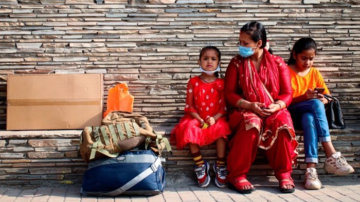 A woman and two young girls sit at a bus station